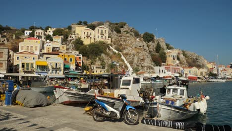 Play-of-sunlight-on-the-boats-moored-in-the-harbour-of-Symi-Island,-Picturesque-background-of-the-town-on-the-hill