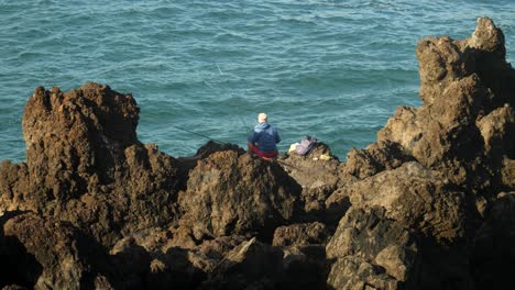 Pescador-Sentado-Sobre-Rocas-En-Puerto-De-La-Cruz