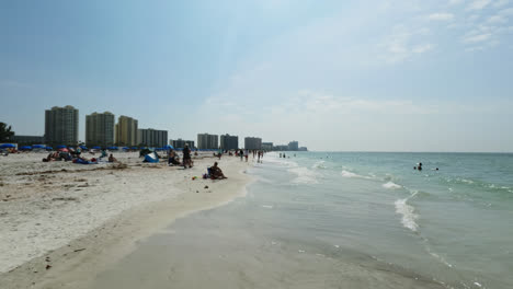 Gente-Caminando-Por-La-Playa-Y-Divirtiéndose-Nadando-En-El-Océano-En-Clearwater-Beach-Con-Hoteles-Al-Fondo,-Florida
