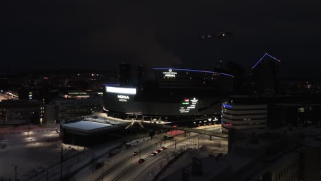 Aerial-view-approaching-the-night-lit-Nokia-areena,-winter-in-Tampere,-Finland