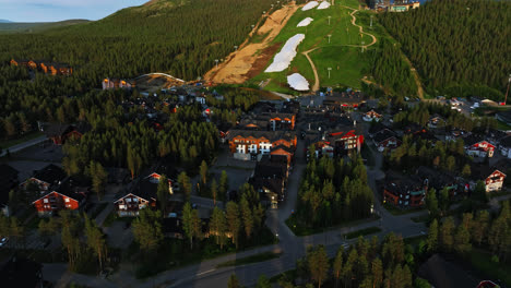 Aerial-view-over-sunlit-buildings-and-slopes-of-Levi,-summer-evening-in-Lapland,-Finland---rotating,-pull-back,-drone-shot
