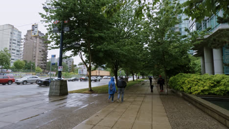 Gente-Caminando-Bajo-La-Lluvia-Con-Paraguas-E-Impermeables-En-Una-Acera-Pavimentada-En-Vancouver,-Canadá