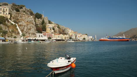 Small-white-and-red-boat-in-the-colorful-harbor-of-Symi-with-panoramic-view-in-background