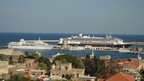 Panoramablick-Auf-Den-Hafen-In-Der-Altstadt-Von-Rhodos,-Gebäude-Und-Grüne-Bäume-Im-Vordergrund,-Kreuzfahrtschiffe-Und-Boote-Im-Hintergrund