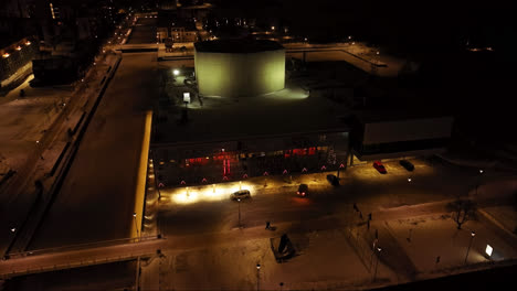 Aerial-pull-back-away-from-the-illuminated-Oulu-Theatre,-winter-night-in-Finland