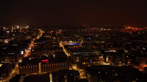 Flying-over-the-night-lit-streets-of-downtown-Oulu,-winter-in-Finland---Aerial-view