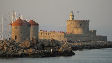 Old-stone-windmills,-fortification-and-lighthouse-in-the-harbor-of-the-Old-Town,-Rhodes