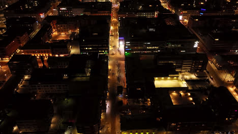 Aerial-view-tilting-over-the-illuminated-streets-of-downtown-Oulu,-winter-night-in-Finland