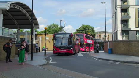 Two-Red-London-Buses-Drive-Through-Pedestrian-Crossing-at-Lewisham-train-Station,-South-East-London