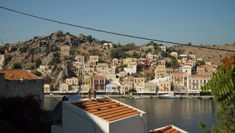 View-on-the-colorful-buildings-on-the-hill-of-Ano-Symi-by-the-harbor,-Houses-and-electrical-cables-in-foreground