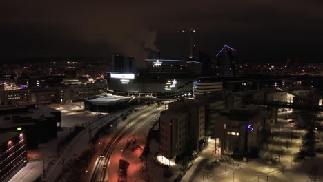 Aerial-view-away-from-the-illuminated-Nokia-arena,-winter-evening-in-Tampere,-Finland---pull-back,-drone-shot