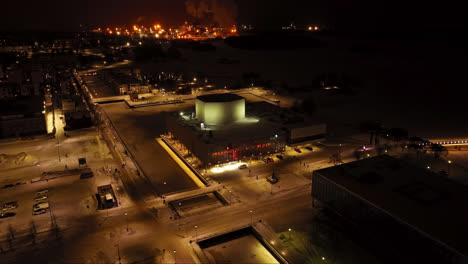 Flying-around-the-illuminated-Oulu-Theatre,-winter-night-in-Finland---Aerial-view