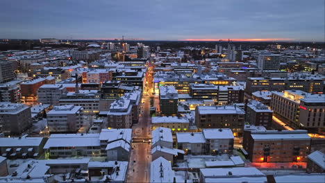 Aerial-view-over-the-snowy-lit-streets-of-Oulu,-dramatic-winter-evening-in-Finland