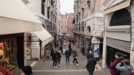 Looking-down-on-the-crowded-street-from-Rialto-Bridge-after-the-cancelled-Carnival,-Many-people-wearing-protective-masks-due-to-coronavirus-outbreak