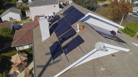 Aerial-slow-orbit-around-three-workers-on-rooftop-installing-and-performing-maintenance-on-multiple-solar-panels-on-a-sunny-day-in-Los-Angeles,-California---orbit,-drone-shot