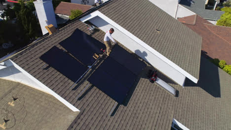 Aerial-quick-orbit-around-a-rooftop-with-workers-installing-and-performing-maintenance-on-multiple-solar-panels-in-Los-Angeles,-California---drone-shot