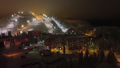 Aerial-view-around-illuminated-Rukatunturi-fell,-winter-evening,-in-Ruka,-Finland---circling,-drone-shot