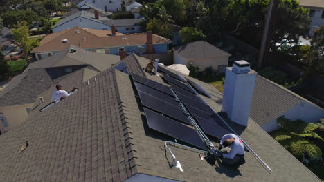Aerial-flyover-rooftop-with-workers-installing-and-performing-maintenance-on-multiple-solar-panels-in-Los-Angeles,-California---drone-shot