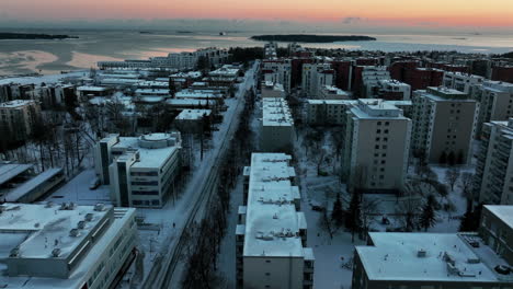 Aerial-view-of-snowy-apartment-buildings-and-the-sun-setting-in-the-sea-in-Lauttasaari,-Helsinki,-Finland