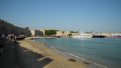 Beach-of-Akti-Sachtouri-and-the-walls-of-the-Old-Town-of-Rhodes,-Yachts-moored-in-the-background
