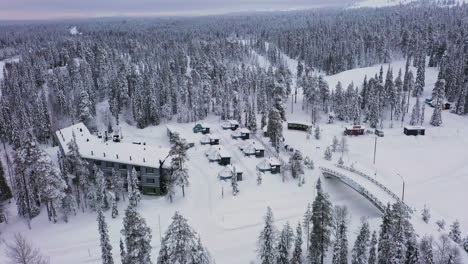 Aerial-view-towards-snowy-northern-lights-huts-at-the-Santa's-Hotel-Aurora,-cloudy-winter-day-in-Lapland
