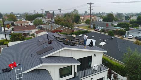 Wide-aerial-parallax-around-two-workers-installing-solar-panels-on-house-roof