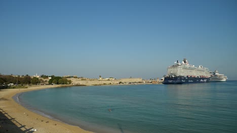 Rhodes-harbour-with-big-cruise-ships-moored,-Sandy-beach-and-the-walls-of-the-Old-Town-in-background