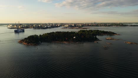 Aerial-view-away-from-the-Pihlajasaari-island-with-the-Eckero-line-ferry-in-the-background,-golden-hour-in-Helsinki,-Finland---pull-back,-drone-shot
