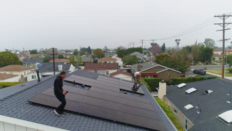 Aerial-view-of-men-installing-photovoltaic-cells-on-a-rooftop---descending,-drone-shot