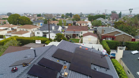 Low-flyover-looking-down-on-workers-installing-solar-panels-on-house-rooftop