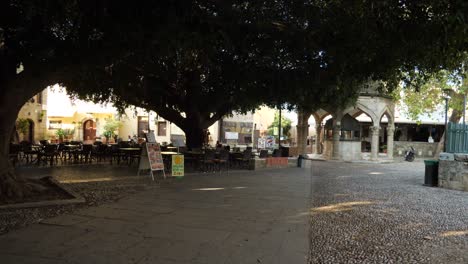 Nearly-empty-restaurant-in-the-square-of-the-Old-Town-of-Rhodes-in-the-shade-of-big-trees