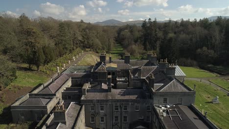 Side-on-aerial-of-Glynllifon-estate-surrounded-by-trees-and-hills-in-the-background
