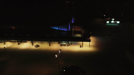 Aerial-view-away-from-the-Jounin-kauppa-market,-winter-night,-in-Akaslompolo,-Finland---pull-back,-drone-shot