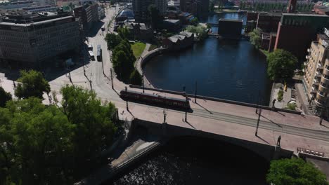Aerial-view-of-a-tram-crossing-a-bridge,-revealing-the-cityscape-of-Tampere,-Finland---tilt,-drone-shot