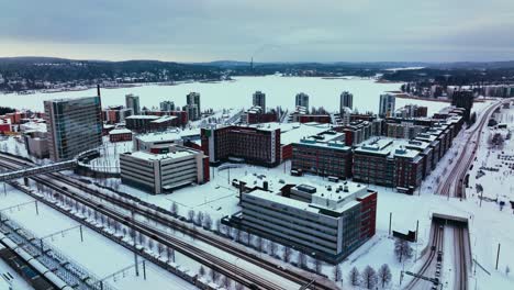 Aerial-view-away-from-the-Lutakko-area-and-over-the-railway-station-in-Jyvaskyla,-winter-evening-in-Finland---pull-back,-drone-shot