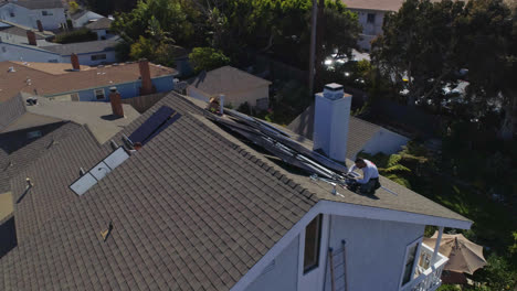 Aerial-orbit-around-rooftop-with-workers-installing-and-performing-maintenance-on-multiple-solar-panels-on-a-sunny-day-in-Los-Angeles,-California---orbit,-drone-shot