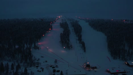 Aerial-view-of-the-illuminated-slopes-of-Saariselka,-gloomy-evening-in-Lapland---tilt,-drone-shot