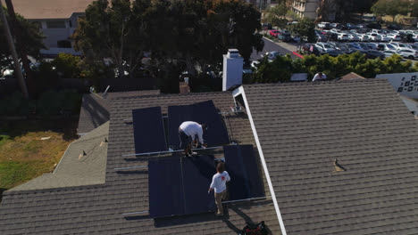 Aerial-orbit-around-workers-on-a-rooftop-are-installing-and-performing-maintenance-on-solar-panels-Los-Angeles,-California---orbit,-drone-shot