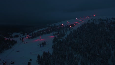 Vista-Aérea-De-Las-Pistas-Iluminadas-Y-El-Centro-De-Esquí-De-Saariselka,-Noche-Polar-En-Laponia---Inclinación,-Disparo-De-Drones