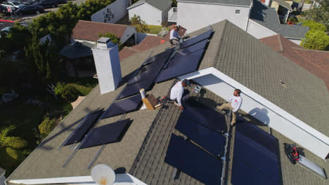 Aerial-orbit-around-three-workers-on-a-rooftop-are-installing-and-performing-maintenance-on-solar-panels-Los-Angeles,-California---orbit,-drone-shot