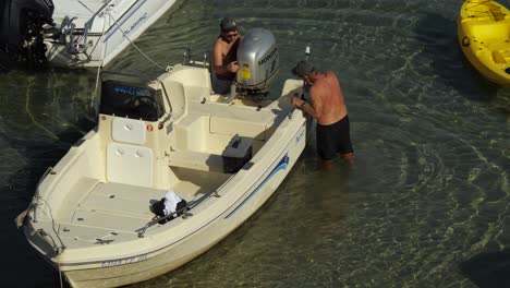 Zwei-Männer-Untersuchen-Den-Motor-Eines-Bootes-Im-Flachen-Meer