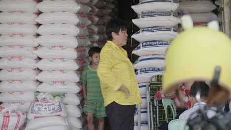 Kids-and-older-women-in-front-of-large-amount-of-big-rice-bag-on-an-outdoor-rice-market-stall-in-Cambodia