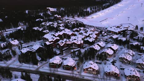 Aerial-view-around-snowy-buildings-in-the-Levi-ski-village,-winter-evening-in-Lapland---circling,-drone-shot
