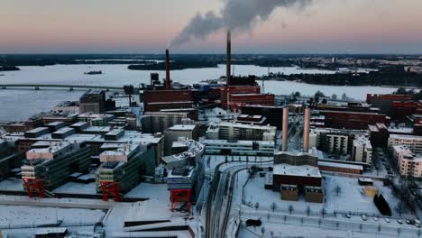 Aerial-view-around-smoking-chimneys-in-Ruoholahti,-winter-sunset-in-Helsinki,-Finland---circling,-drone-shot