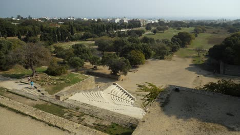 Vista-De-ángulo-Alto-Del-Antiguo-Teatro-En-La-Acrópolis-De-Rodas,-La-Ciudad-De-Rodos-Al-Fondo