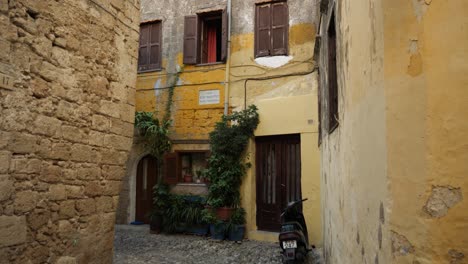 Traditional-yellow-painted-houses,-stone-wall-and-rocky-road-in-the-Old-Town-of-Rhodes