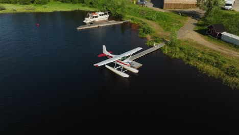 Aerial-view-in-front-of-a-seaplane-docked-at-a-lake-pier,-summer-in-Inari,-Finland---descending,-tilt,-drone-shot