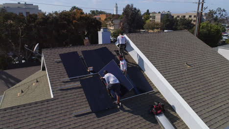 Aerial-slow-orbit-around-three-workers-on-a-rooftop-installing-and-performing-maintenance-on-solar-panels-Los-Angeles,-California---orbit,-drone-shot