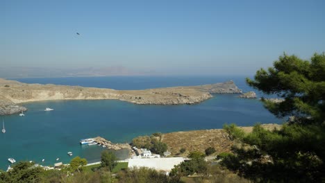 The-bay-at-Lindos-with-Pallas-Beach-and-small-islets-in-background,-Pine-tree-in-foreground