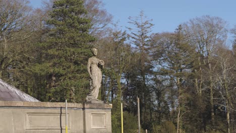 Aerial-close-up-of-a-statue-on-the-roof-of-the-Glynllifon-estate-with-sky-and-trees-in-the-background